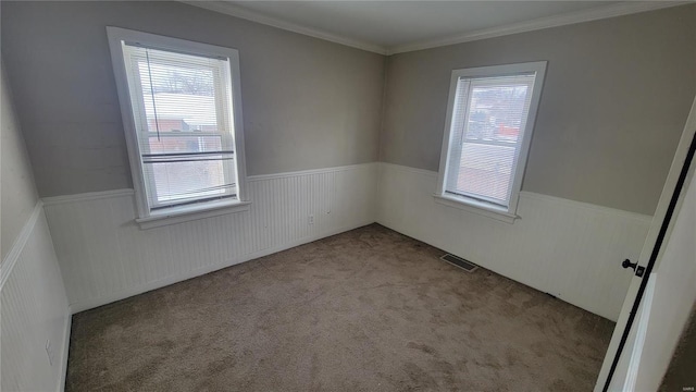 unfurnished room with wainscoting, crown molding, visible vents, and carpet flooring