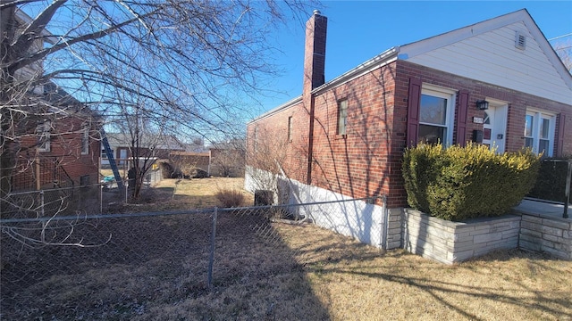 view of side of home with a yard, brick siding, a chimney, and fence