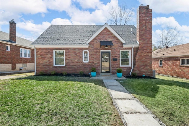 view of front of house featuring brick siding, a chimney, a front yard, and a shingled roof