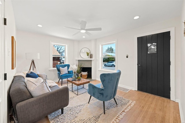 living room featuring light wood-style flooring, a fireplace, baseboards, and a healthy amount of sunlight