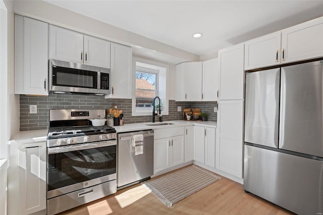 kitchen featuring a sink, light countertops, light wood-style floors, appliances with stainless steel finishes, and white cabinetry