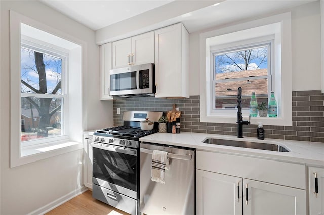 kitchen with a sink, white cabinets, tasteful backsplash, and stainless steel appliances