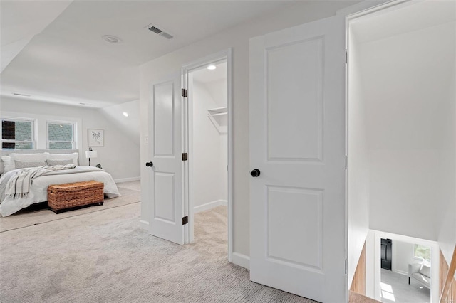 bedroom featuring visible vents, a walk in closet, baseboards, light colored carpet, and lofted ceiling