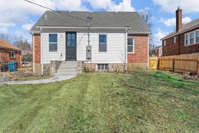 rear view of house with a yard, brick siding, a shingled roof, and fence