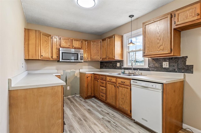 kitchen featuring light wood finished floors, stainless steel microwave, hanging light fixtures, a sink, and dishwasher