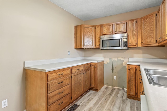 kitchen featuring light wood finished floors, brown cabinetry, stainless steel microwave, light countertops, and a textured ceiling