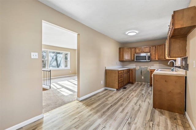 kitchen featuring baseboards, stainless steel microwave, a sink, and brown cabinets