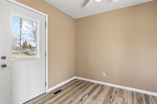 doorway featuring ceiling fan, light wood-style floors, visible vents, and baseboards