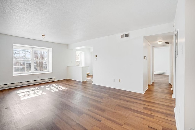 unfurnished living room featuring visible vents, baseboard heating, wood finished floors, and a textured ceiling