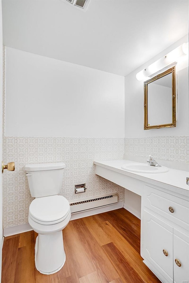 bathroom with wallpapered walls, toilet, baseboard heating, wood finished floors, and vanity