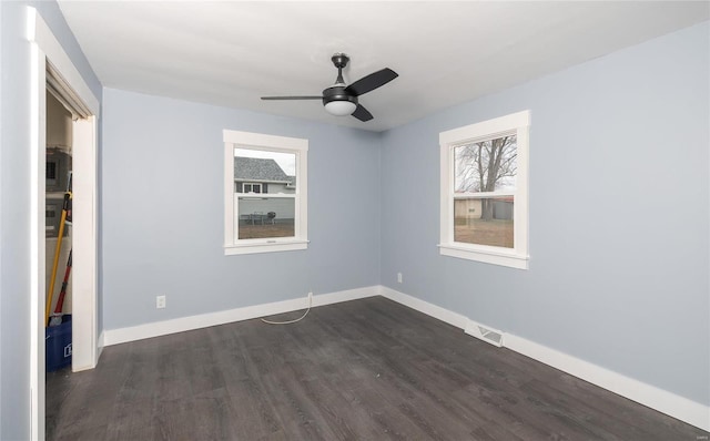 unfurnished room with dark wood-style floors, visible vents, baseboards, and a ceiling fan