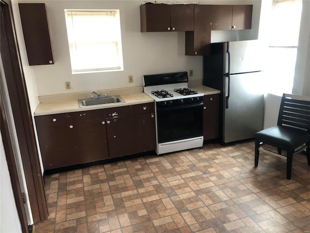 kitchen featuring dark brown cabinetry, light countertops, freestanding refrigerator, gas stove, and a sink