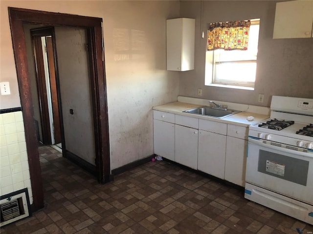 kitchen featuring light countertops, white cabinets, gas range gas stove, and a sink