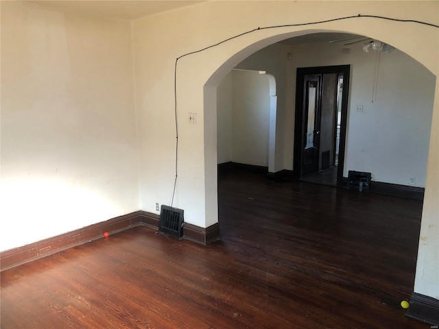 empty room with arched walkways, visible vents, baseboards, and wood finished floors