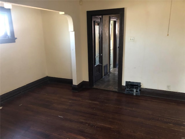 empty room with baseboards, dark wood-style flooring, and arched walkways