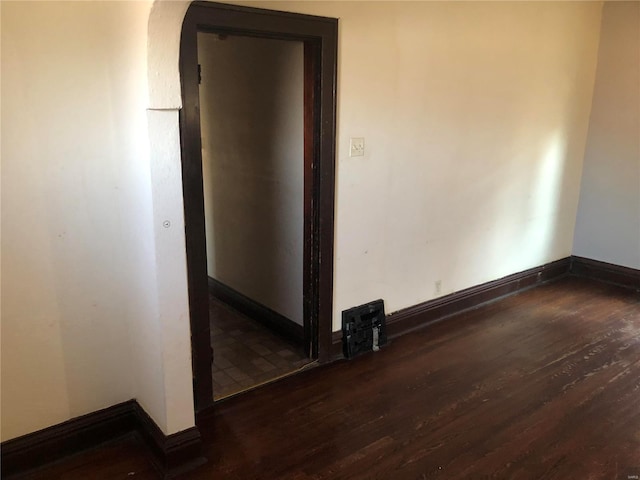 empty room featuring baseboards, arched walkways, and wood finished floors