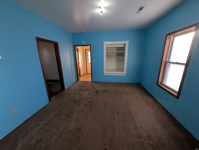 spare room featuring a textured ceiling, built in shelves, carpet flooring, and visible vents