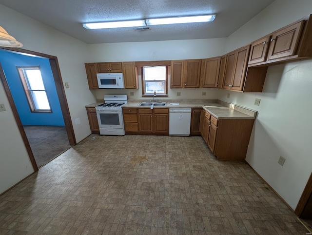 kitchen with white appliances, visible vents, brown cabinets, light countertops, and a sink