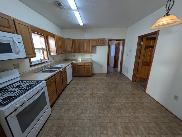 kitchen featuring decorative light fixtures, visible vents, brown cabinetry, a sink, and white appliances