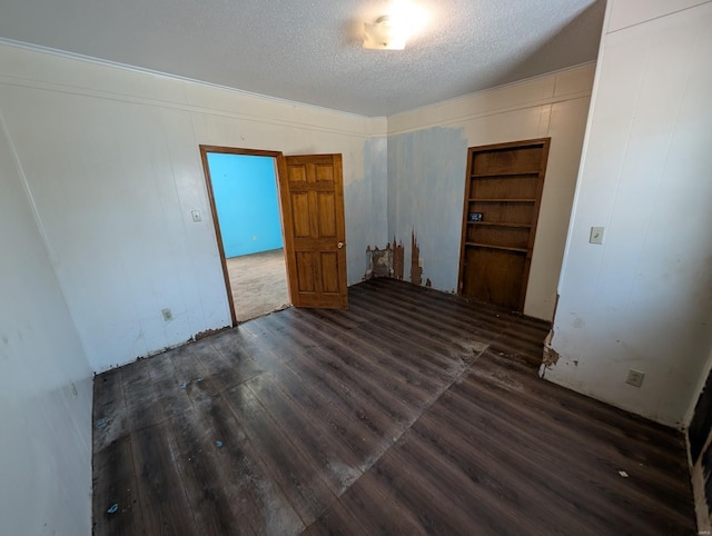 unfurnished room with built in shelves, dark wood-type flooring, and a textured ceiling