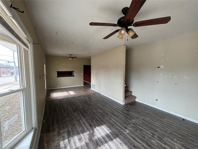 unfurnished living room featuring dark wood-style floors, baseboards, stairway, and ceiling fan