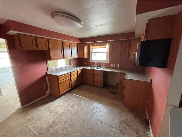 kitchen with a textured ceiling, stainless steel microwave, brown cabinetry, and a sink