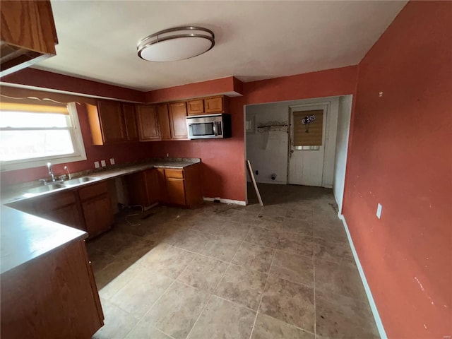 kitchen featuring baseboards, stainless steel microwave, brown cabinets, and a sink