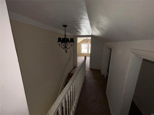 corridor featuring lofted ceiling, dark colored carpet, a textured ceiling, and a notable chandelier