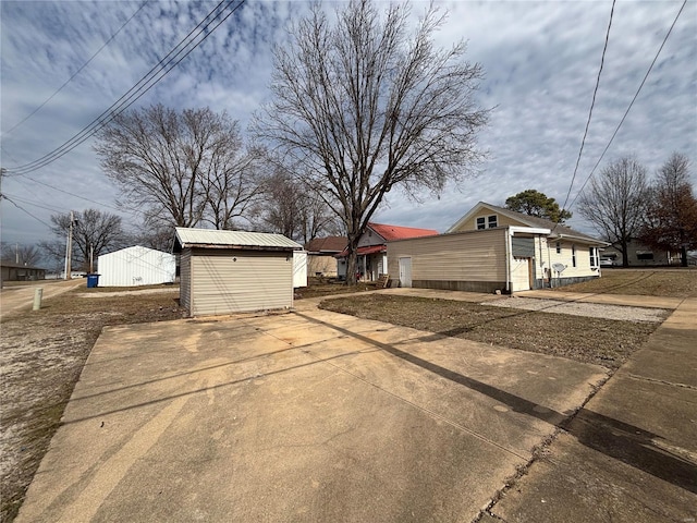 view of side of home with driveway, a storage shed, metal roof, an outbuilding, and an attached garage