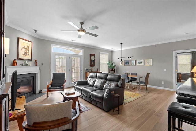 living area with light wood finished floors, baseboards, a fireplace with flush hearth, ceiling fan, and crown molding