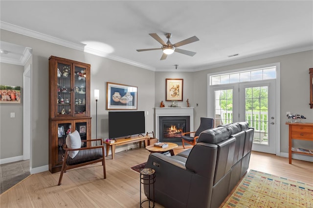 living room with light wood finished floors, baseboards, ornamental molding, and a glass covered fireplace