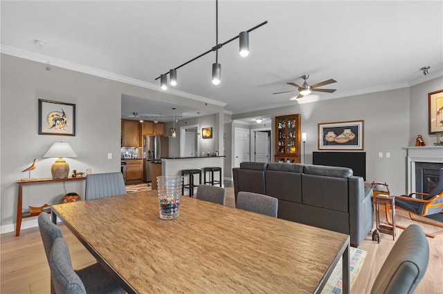 dining space with ornamental molding, a glass covered fireplace, light wood-style floors, a ceiling fan, and track lighting