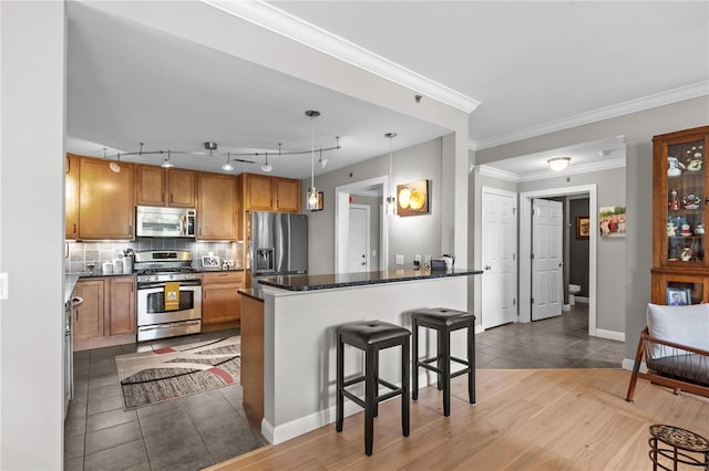 kitchen with stainless steel appliances, tasteful backsplash, hanging light fixtures, brown cabinetry, and a kitchen breakfast bar