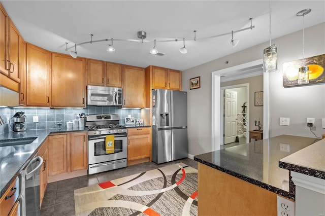 kitchen with dark tile patterned flooring, a sink, appliances with stainless steel finishes, backsplash, and pendant lighting