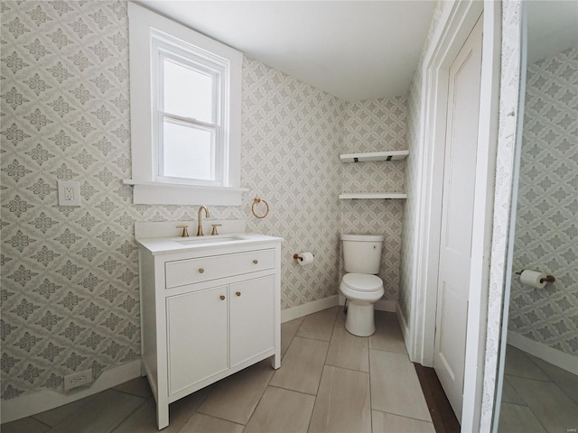 bathroom with tile patterned flooring, toilet, vanity, baseboards, and wallpapered walls