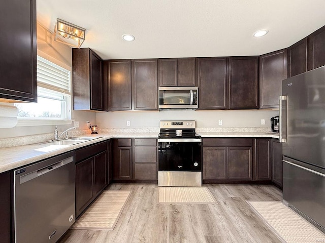 kitchen with light countertops, appliances with stainless steel finishes, a sink, dark brown cabinets, and light wood-type flooring