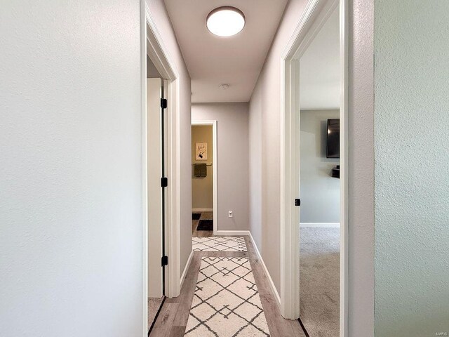 hallway featuring light wood finished floors and baseboards