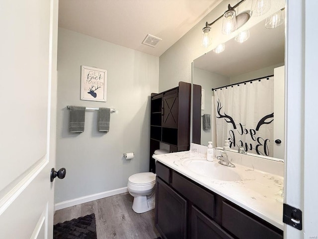 bathroom featuring baseboards, visible vents, toilet, wood finished floors, and vanity