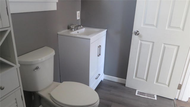 half bathroom with toilet, wood finished floors, vanity, visible vents, and baseboards