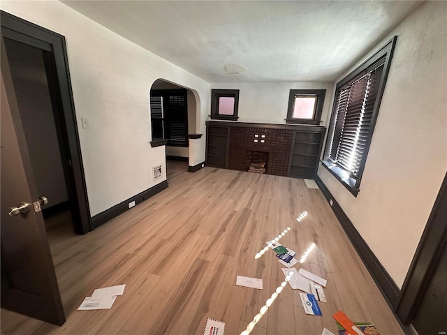 living area featuring light wood-style floors, a brick fireplace, visible vents, and baseboards