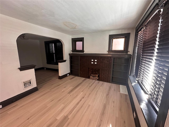 unfurnished living room featuring arched walkways, visible vents, a brick fireplace, wood finished floors, and baseboards