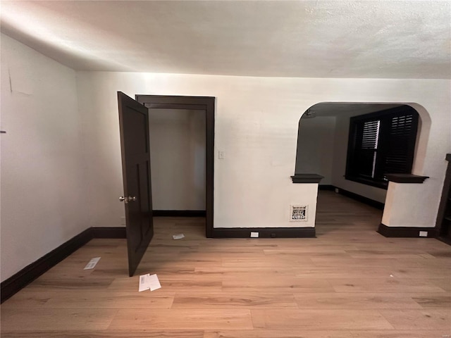 spare room featuring light wood-type flooring, baseboards, visible vents, and arched walkways