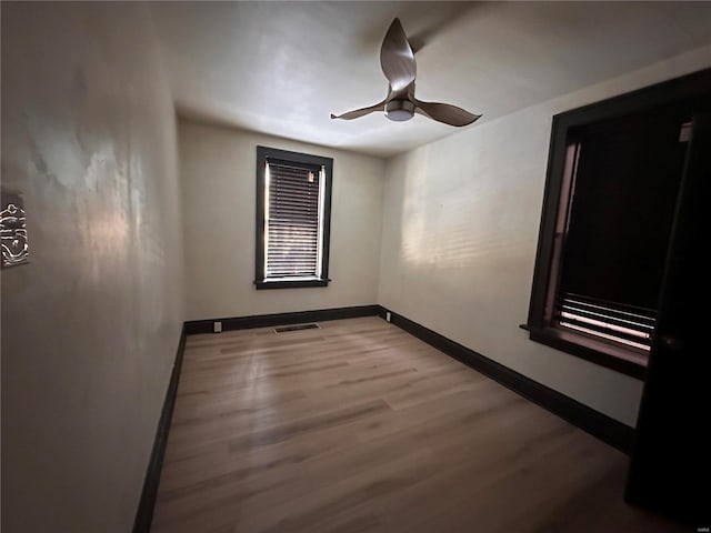 empty room featuring a ceiling fan, wood finished floors, visible vents, and baseboards