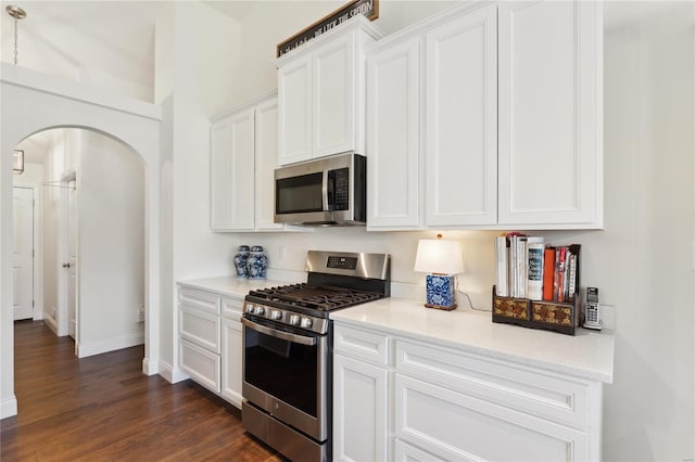 kitchen with dark wood-style floors, baseboards, arched walkways, stainless steel appliances, and white cabinetry