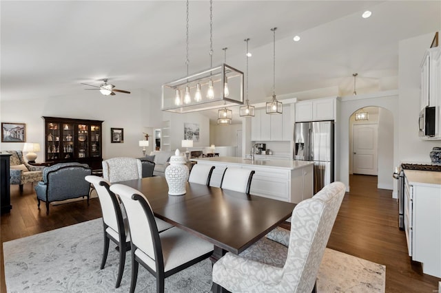 dining space featuring arched walkways, dark wood-style flooring, ceiling fan, and vaulted ceiling