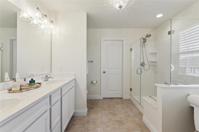 full bath featuring baseboards, double vanity, a sink, a shower stall, and a chandelier