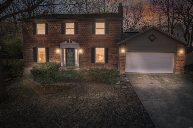 colonial home with concrete driveway, brick siding, a chimney, and an attached garage