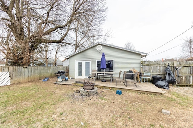 rear view of property with a fire pit, a lawn, a fenced backyard, a deck, and french doors