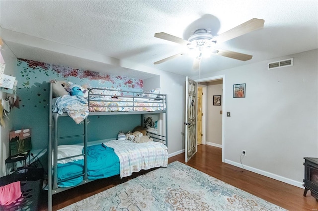 bedroom featuring baseboards, visible vents, ceiling fan, wood finished floors, and a textured ceiling