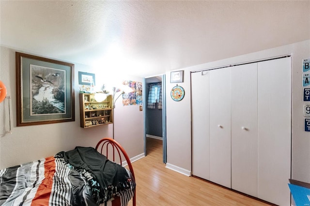 bedroom featuring a closet, baseboards, light wood-style flooring, and a textured ceiling